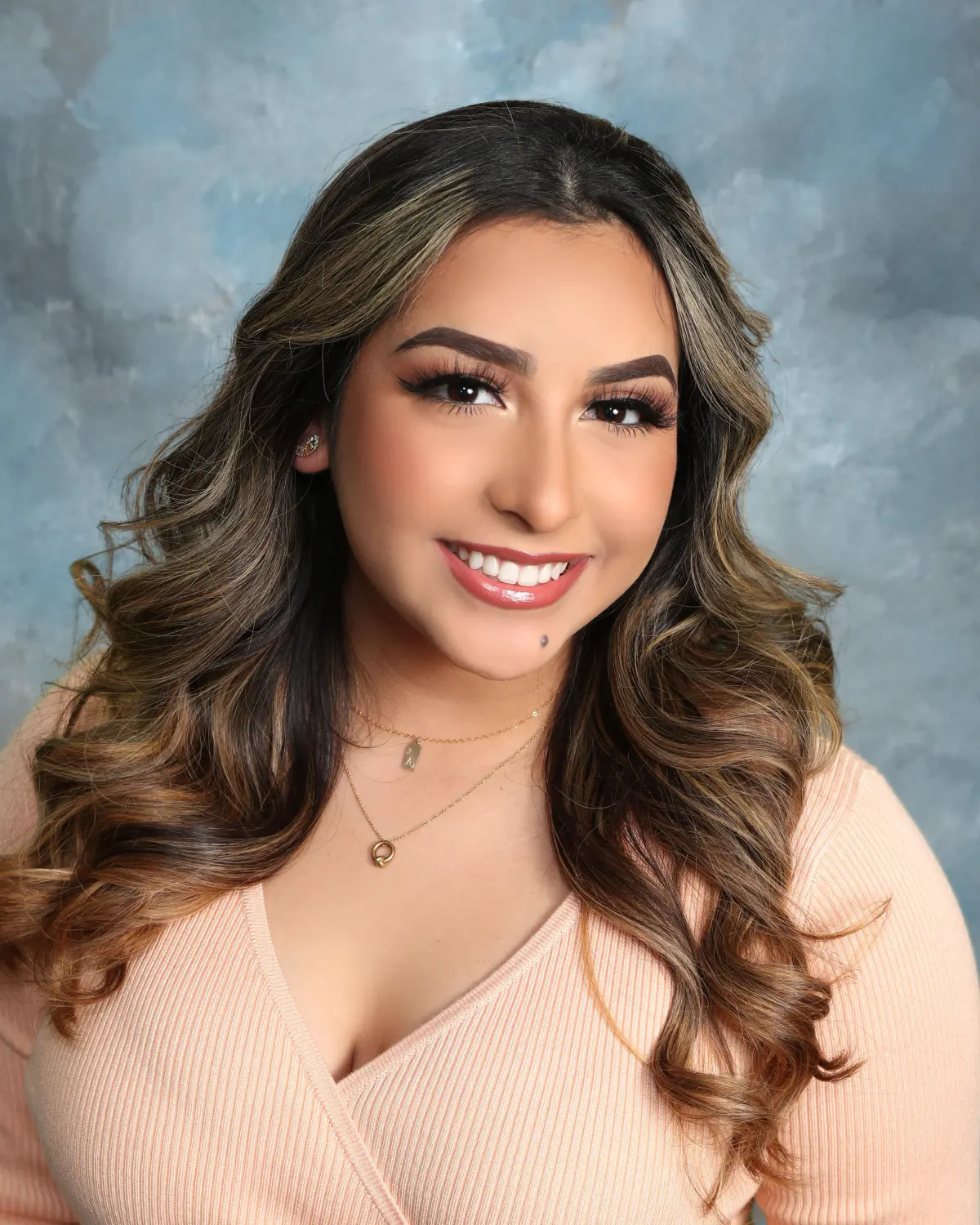 Young woman with long highlighted brunette waves, blush wrap top, delicate necklace, big smile