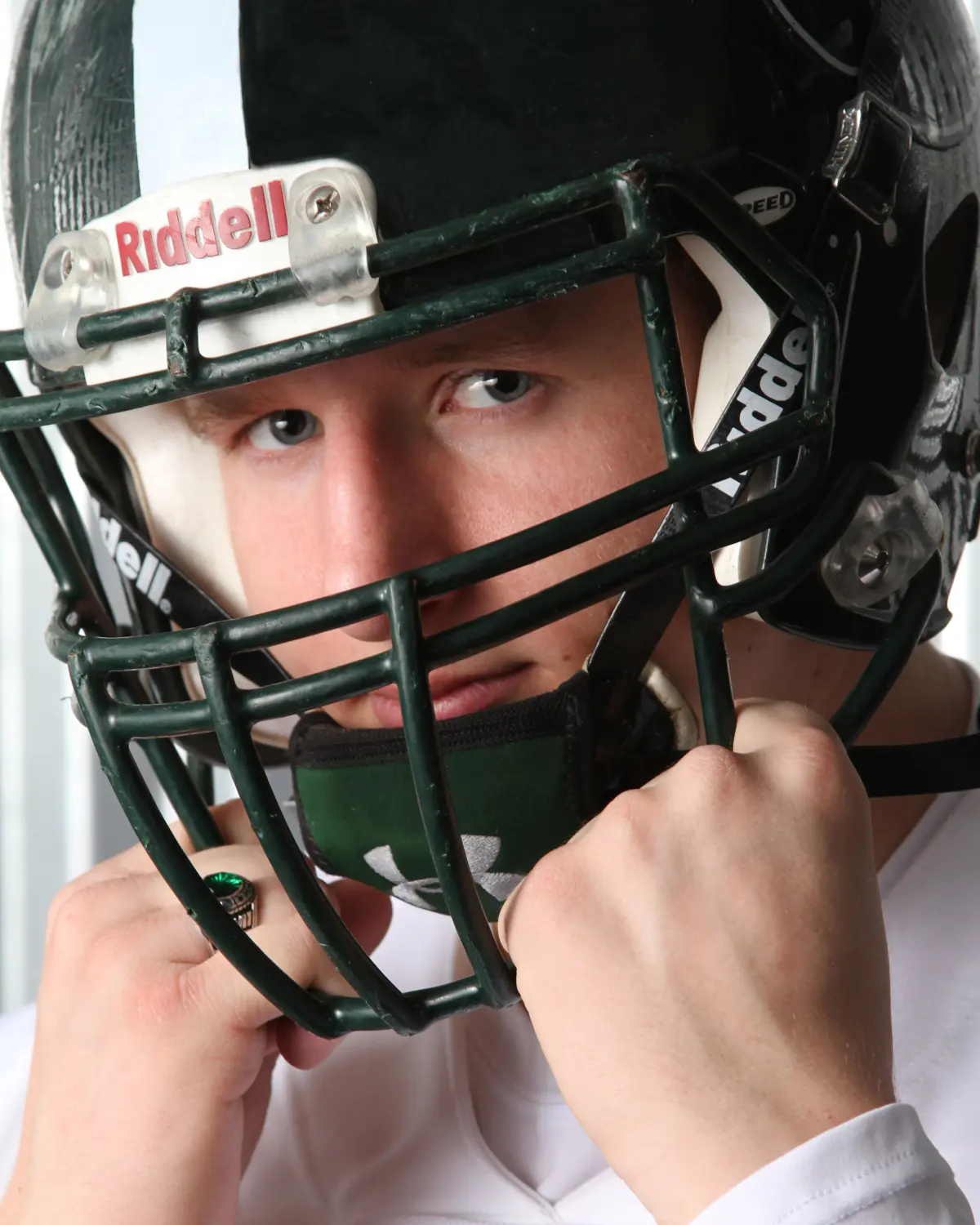 Extreme close-up of a football player behind a green Riddell helmet facemask, fists gripping the bars, intense sideways look