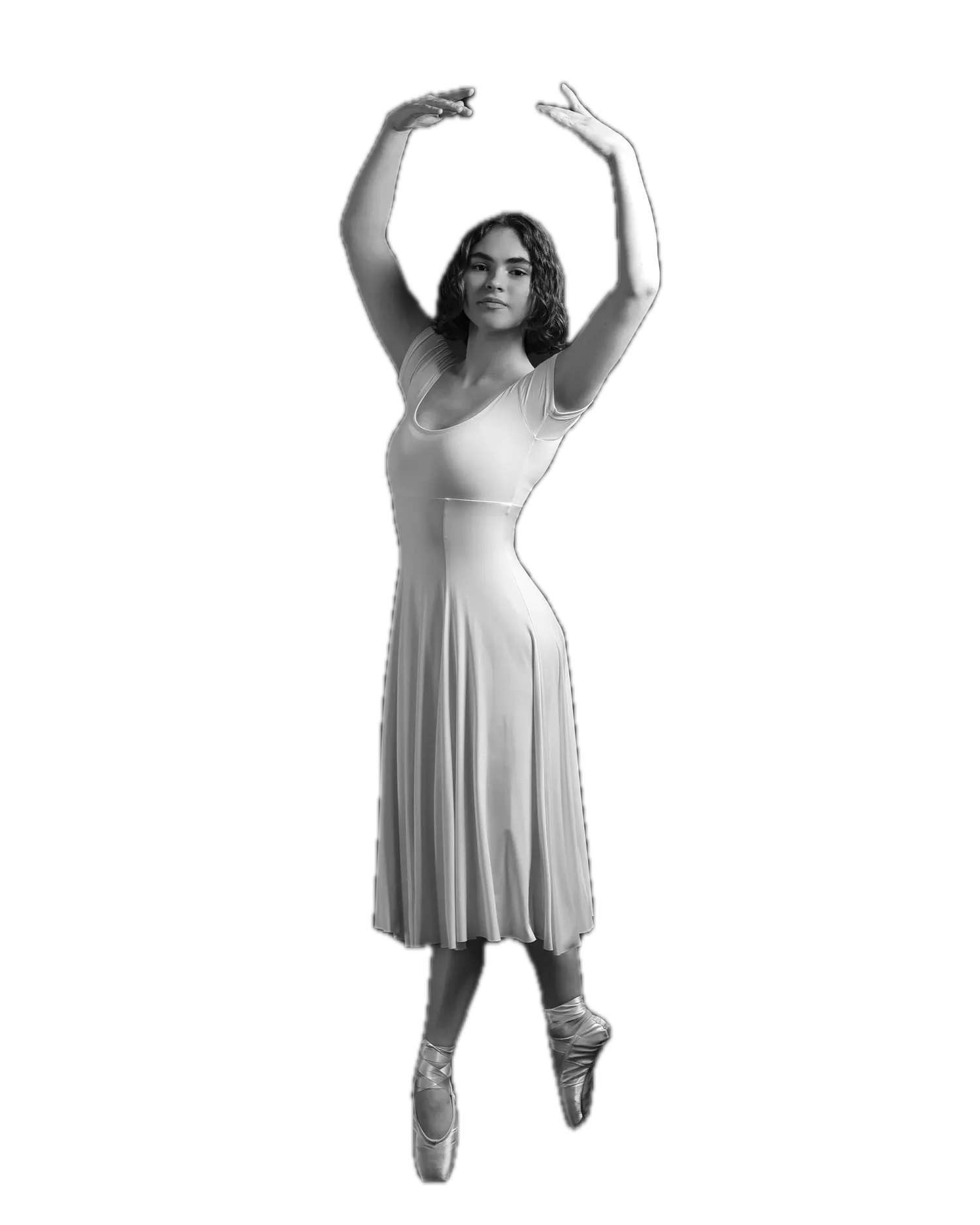 Black-and-white full-length portrait of a young dancer en pointe in a pale fitted dance dress, both arms raised overhead in a ballet position