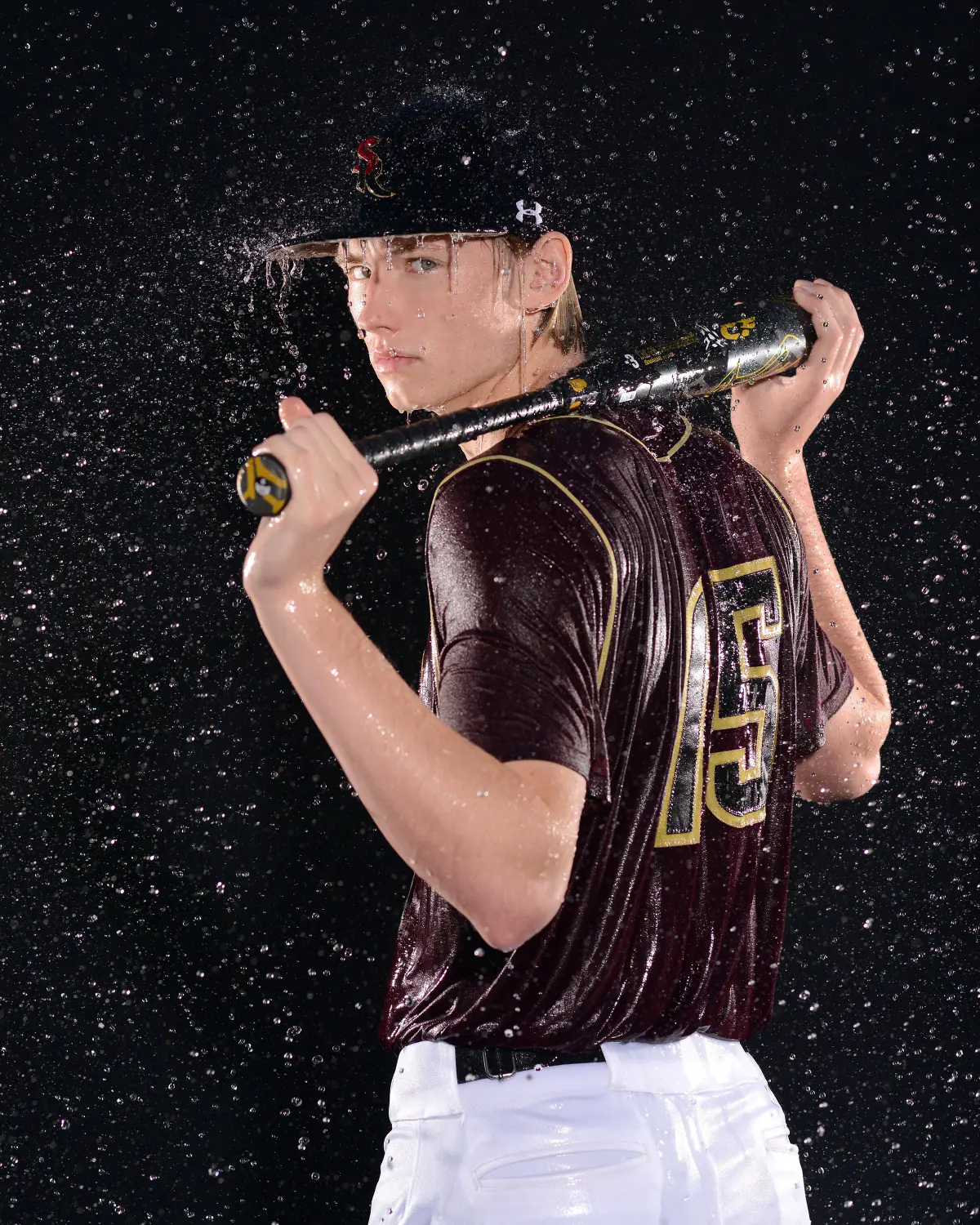 Senior baseball player photographed with water splashing, looking back over his shoulder