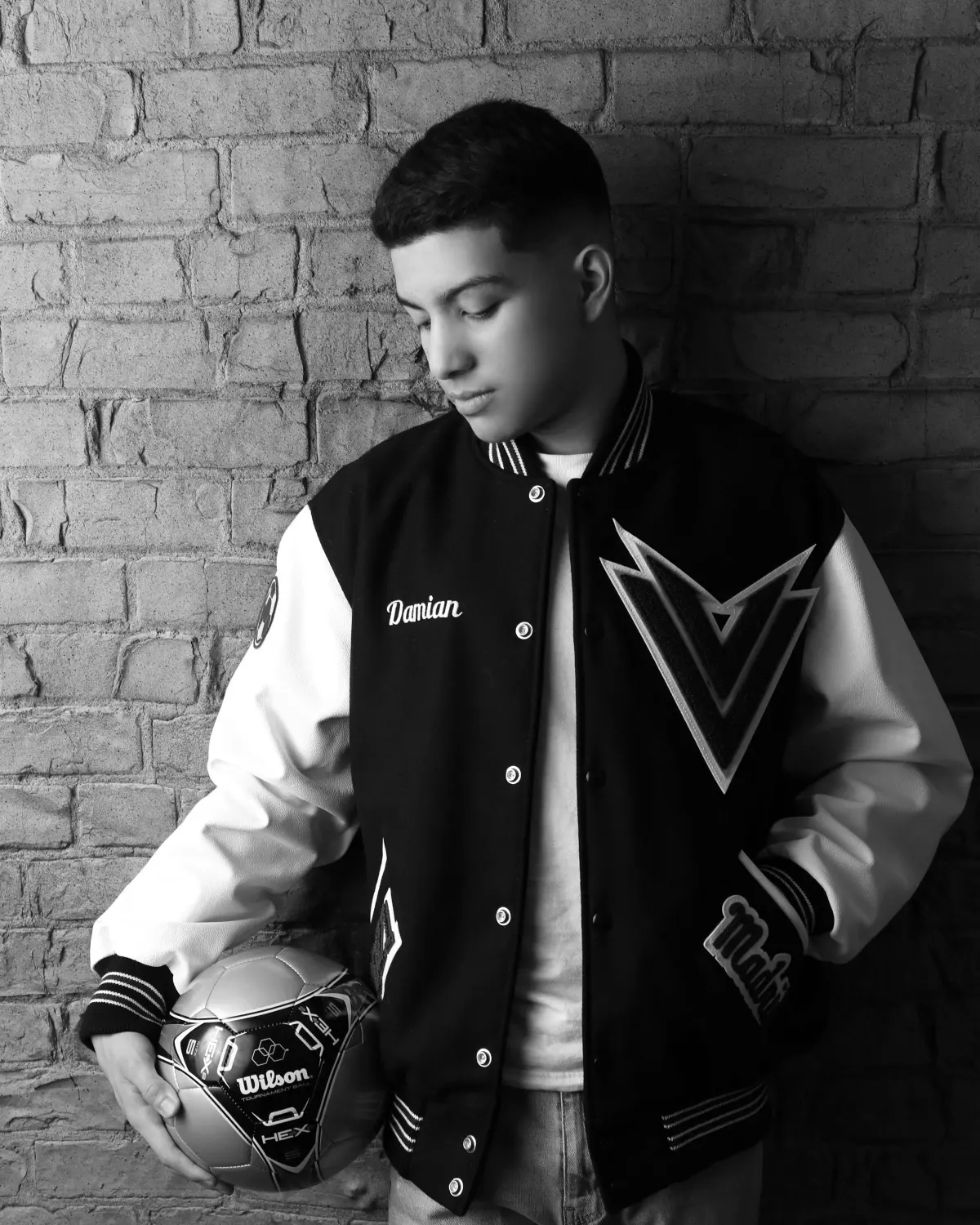 Senior in a letterman jacket with a soccer ball, black and white