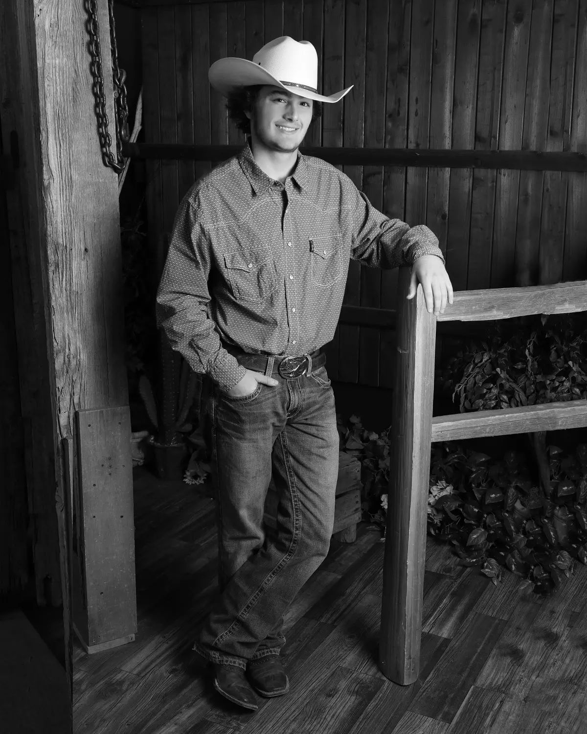 Black-and-white full-length portrait of a young man in a cowboy hat, western snap shirt, jeans and boots