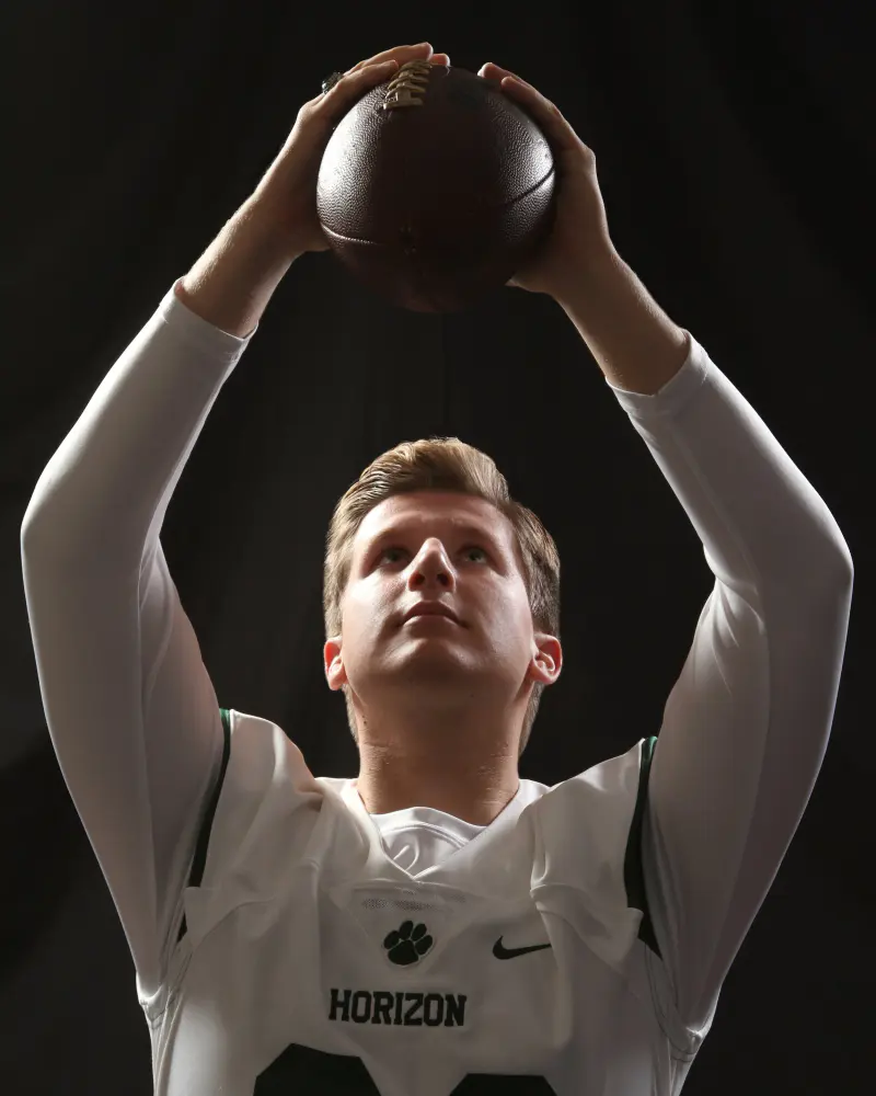Football player holding the ball overhead, on black