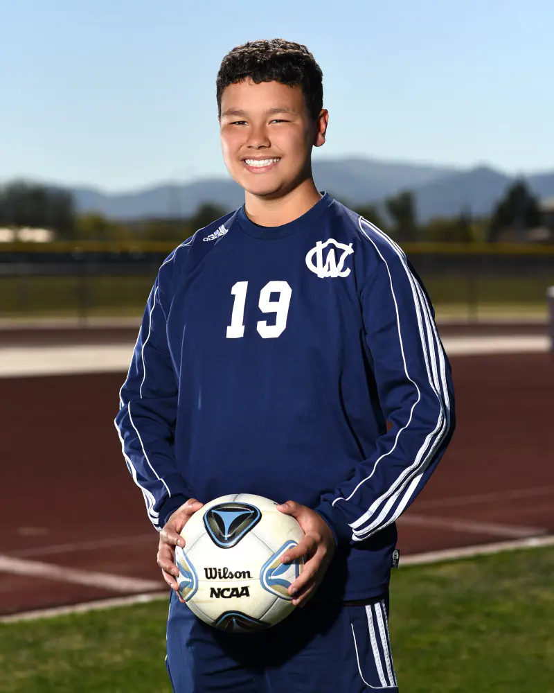Soccer player holding the ball on a track, mountains behind