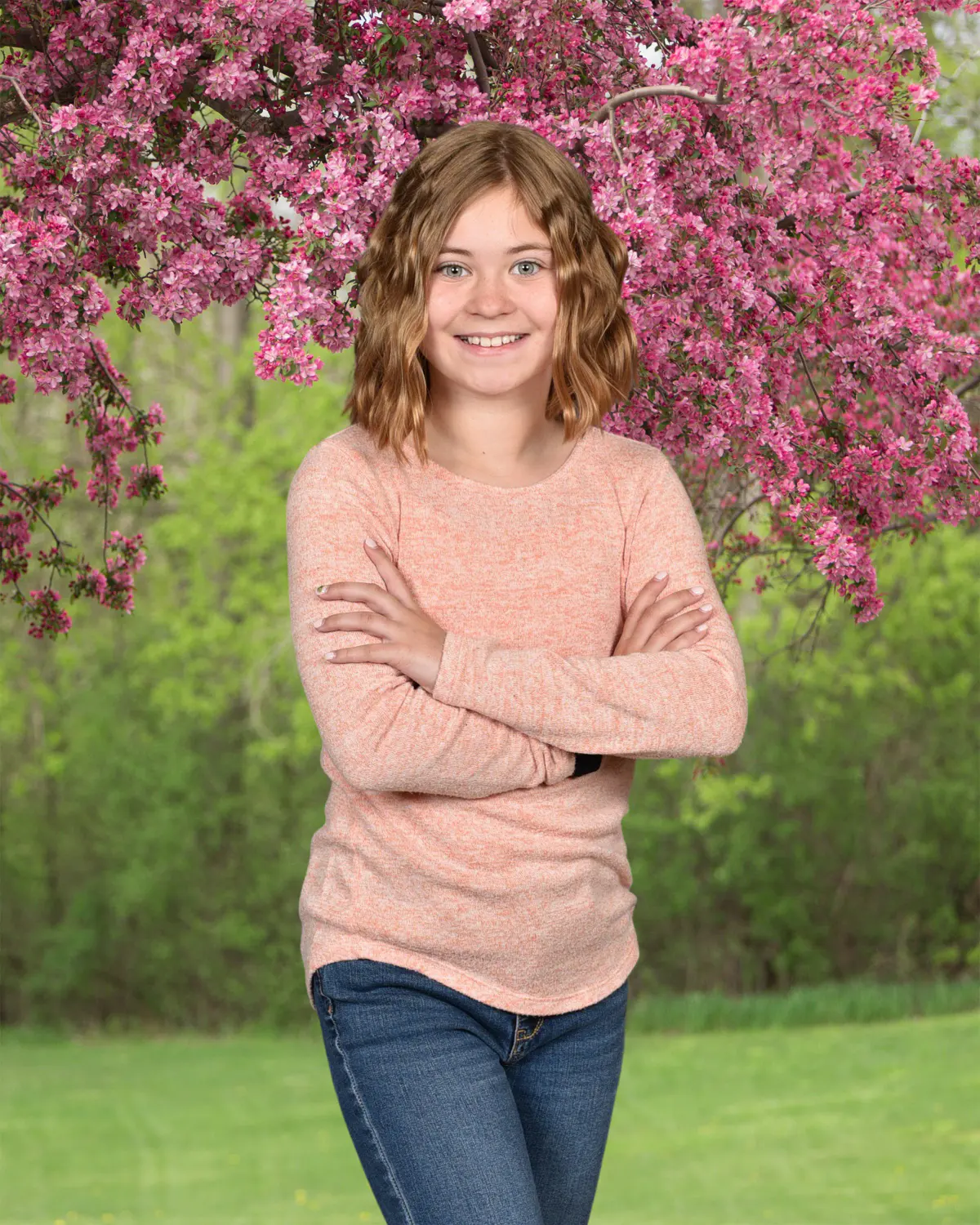 Girl with shoulder-length wavy hair in a peach sweater and jeans, arms crossed, smiling
