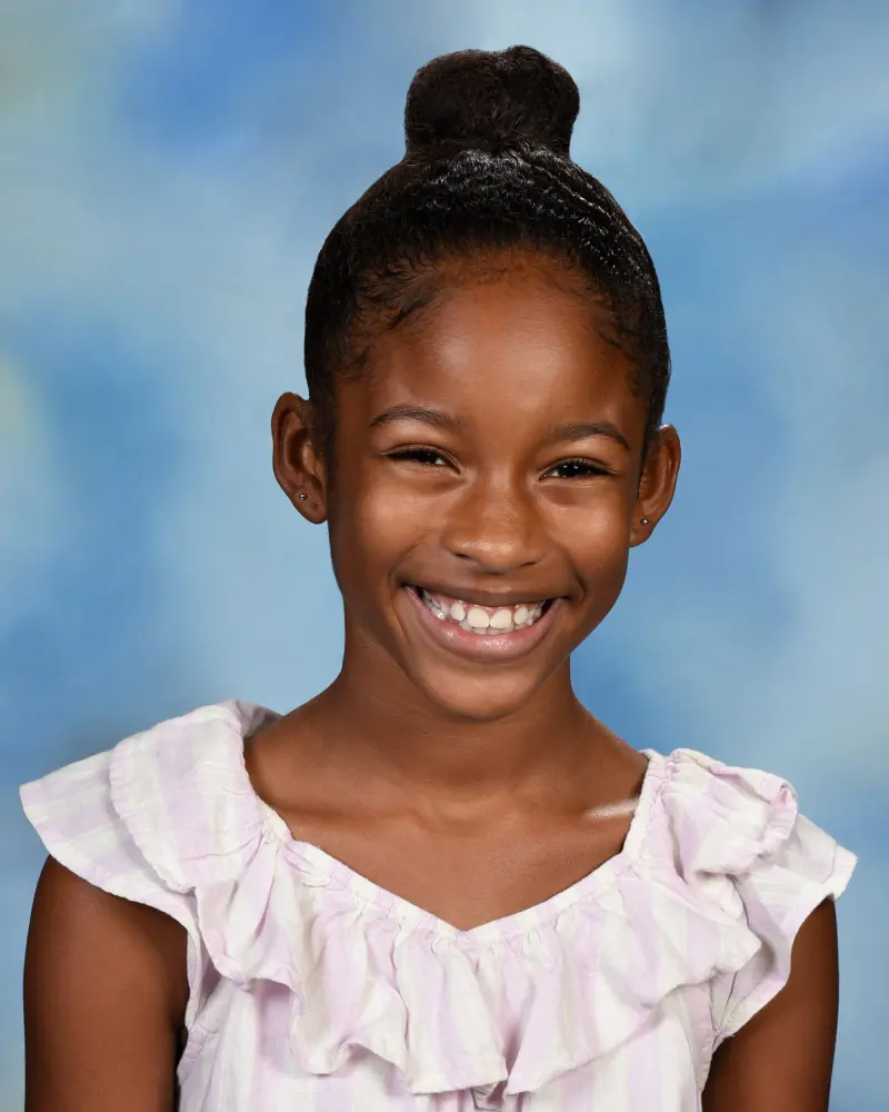 School portrait of a laughing girl with her hair in a top bun on a light blue backdrop