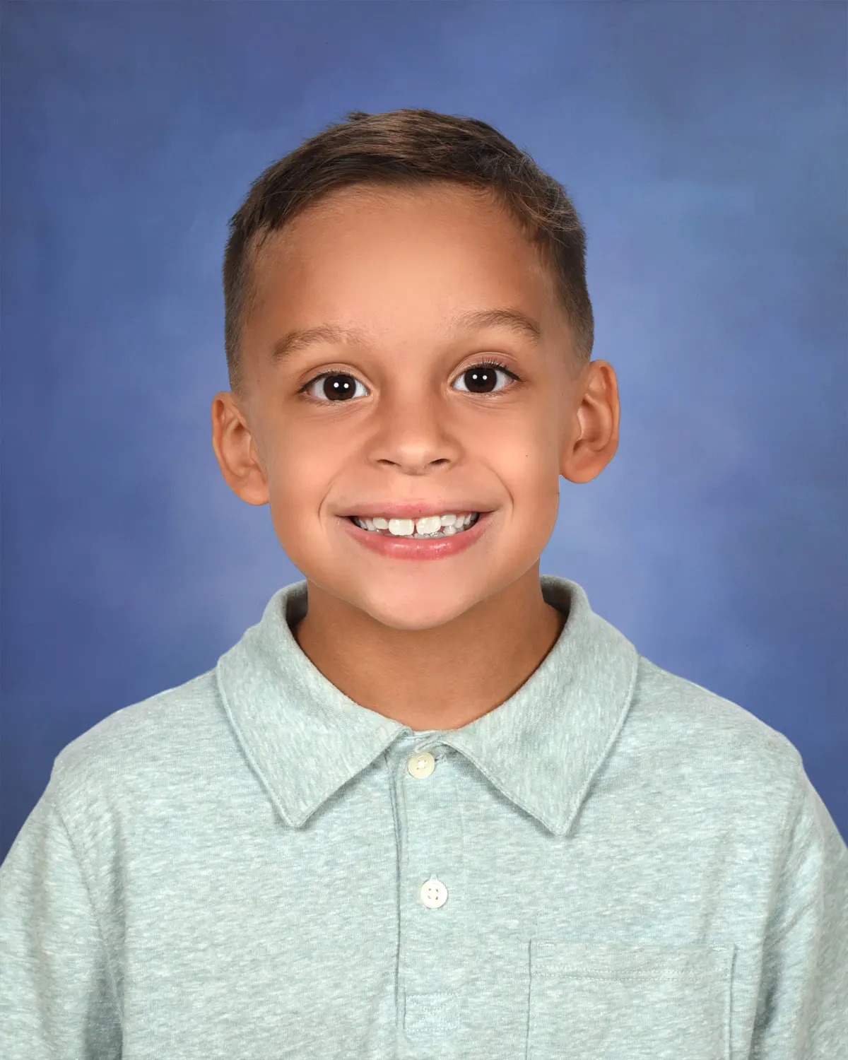 Boy in a mint knit polo with a wide smile, on a blue mottled backdrop