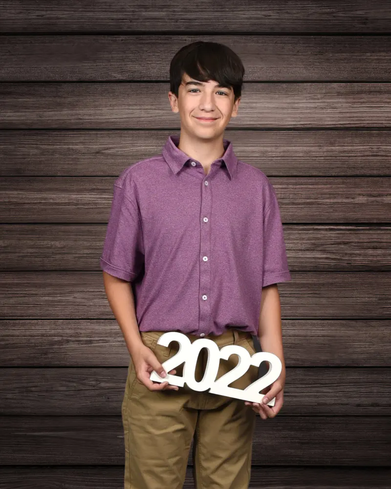 School portrait of a smiling preteen boy in a purple polo on a wood backdrop