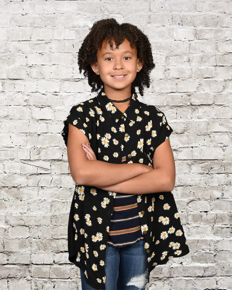 School portrait of a smiling girl with curly hair on a white brick backdrop