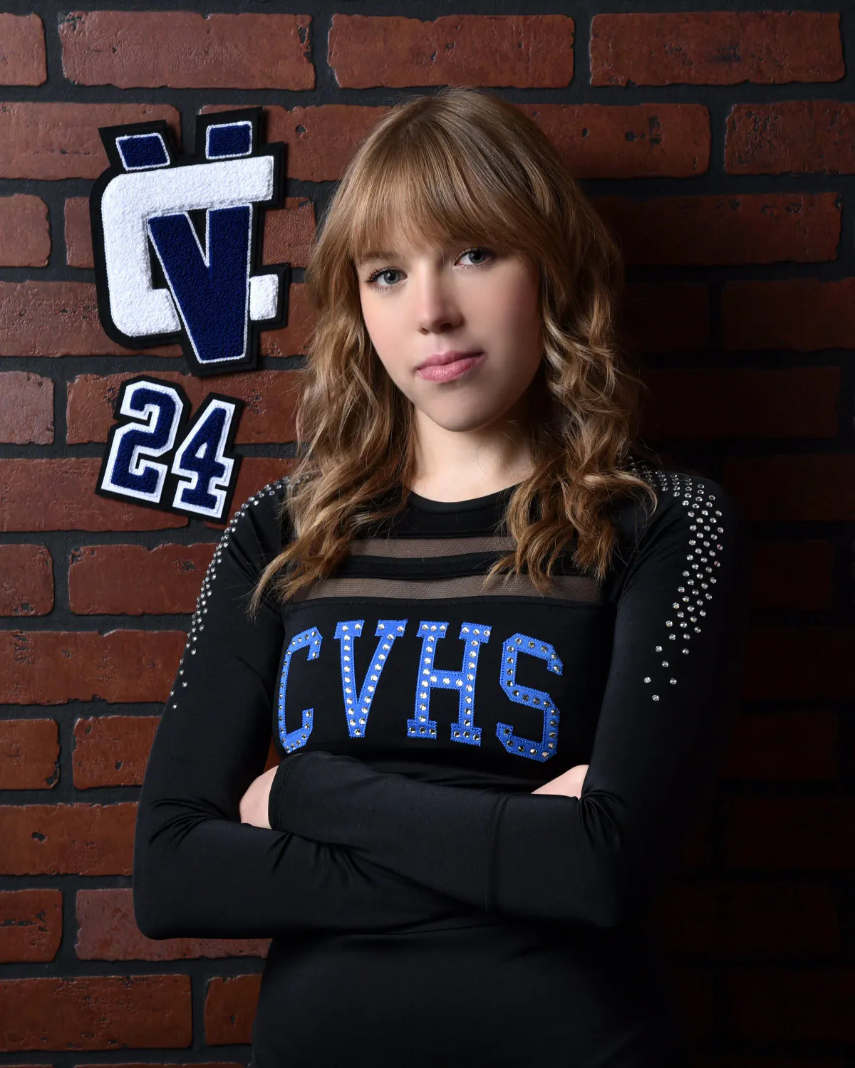 Young woman in black long-sleeve pom/cheer uniform with rhinestone 'CVHS', arms crossed