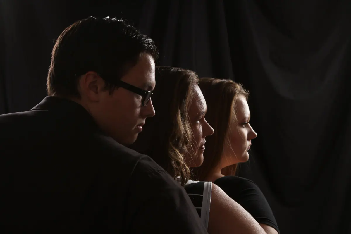 Three people in staggered profile facing right (young man with glasses in front, two women behind)