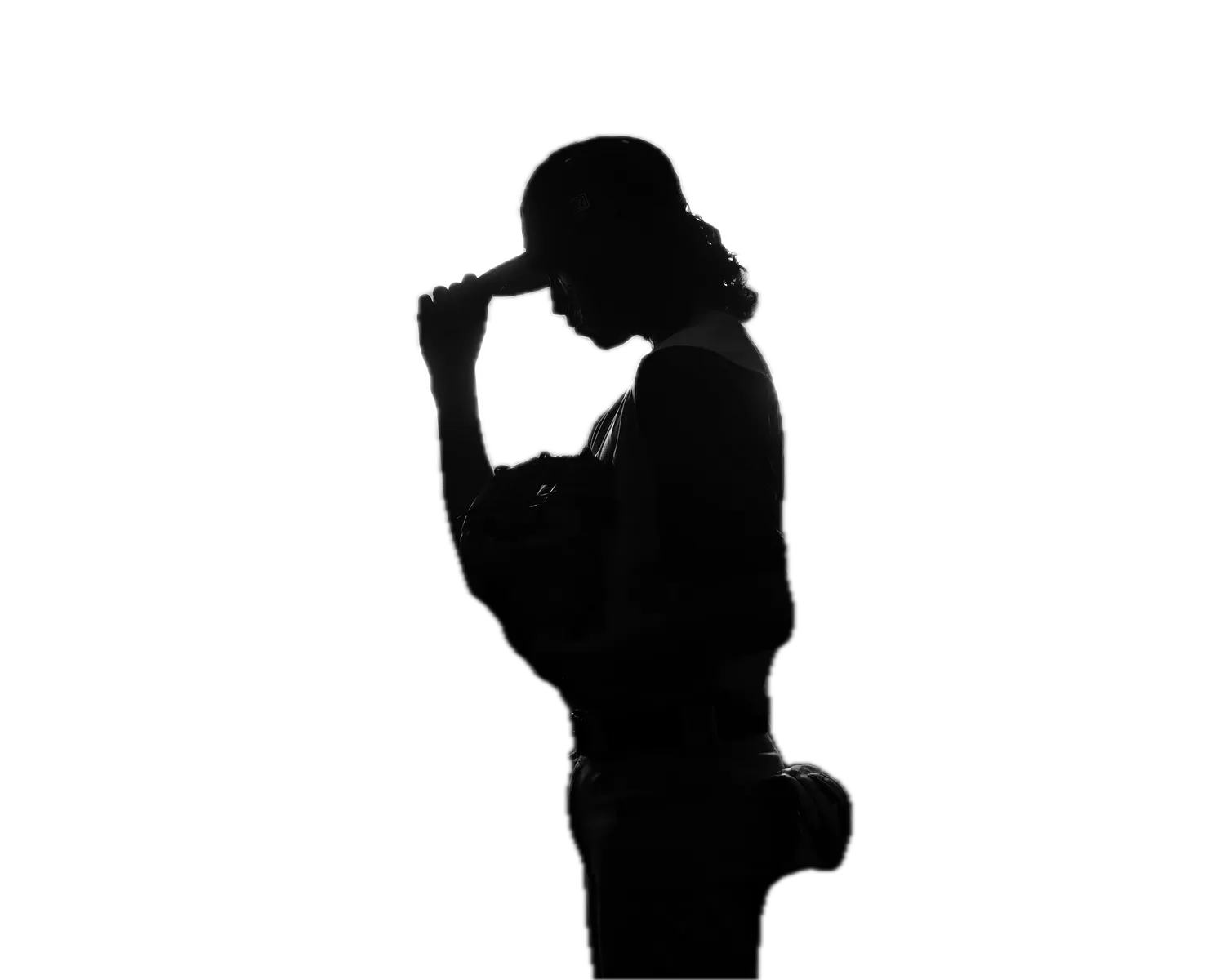 Baseball player in silhouette tipping his cap, backlit by stadium-style lights and haze