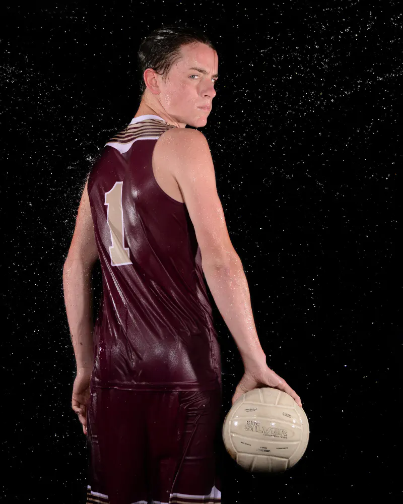 Athlete looking back over his shoulder with a volleyball, water spray on black