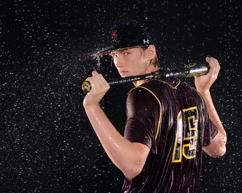 Baseball player with a bat across his shoulders, water spraying off his cap