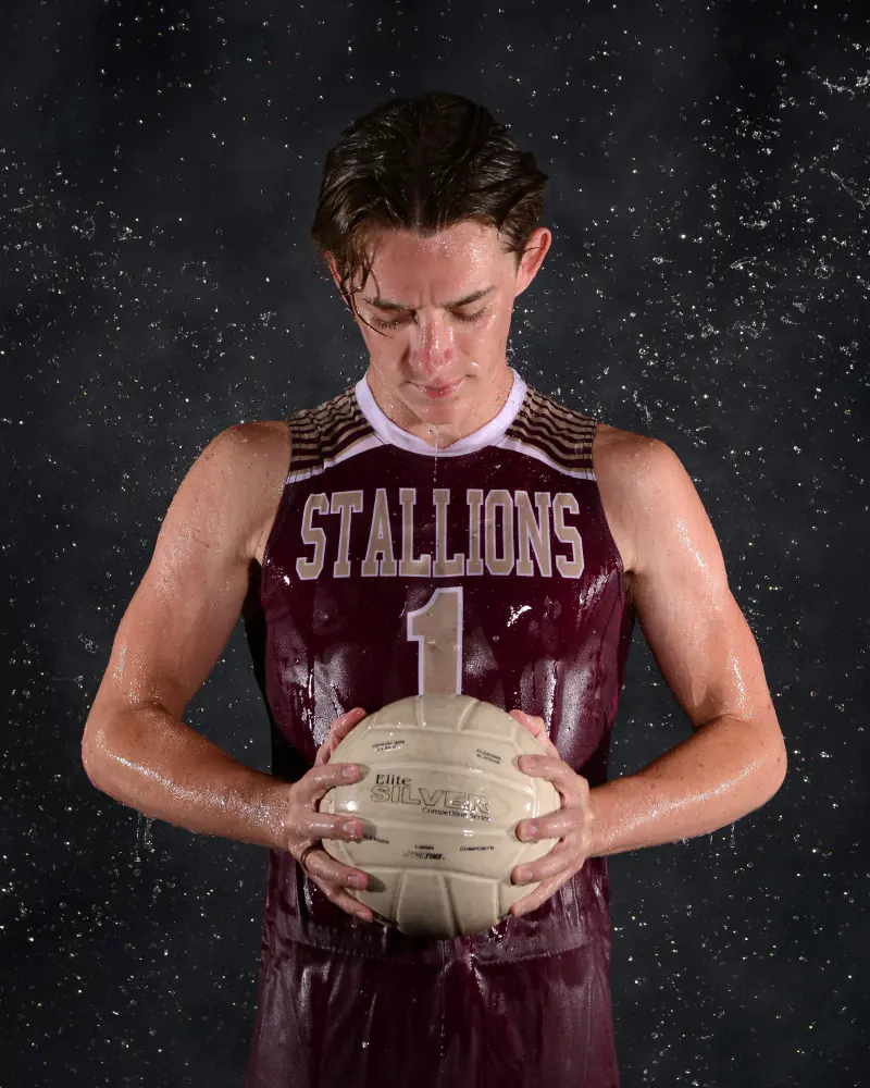 Volleyball player with head bowed, holding the ball, water droplets